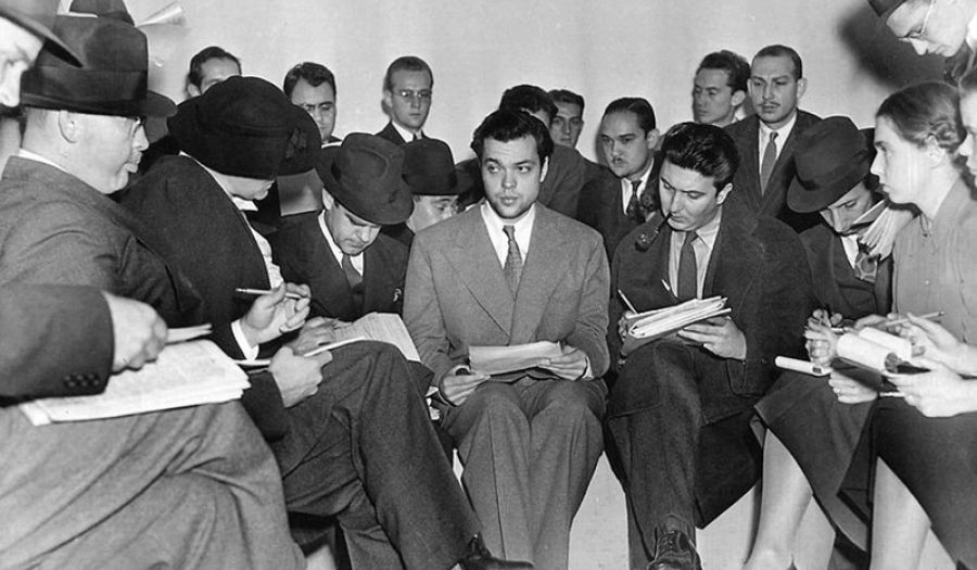 Orson Welles (center) meeting with reporters after the <i>War of the Worlds</i> radio broadcast. November, 1938. CREDIT: <a href="https://commons.wikimedia.org/wiki/File:Orson_Welles_1938_War_of_the_Worlds.jpg">The Express (Public Domain)</a>